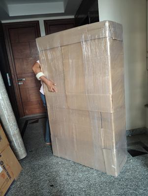 A crew member carrying a large wrapped flat item through a doorway.