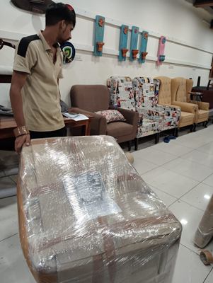 A crew member standing beside a wrapped armchair in a furnished living room.