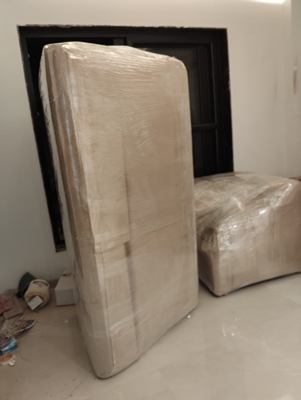 A wrapped mattress and a wrapped ottoman standing beside a doorway.