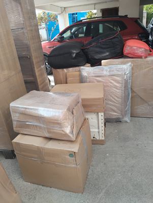 Cartons and wrapped goods gathered in a garage beside a parked car.