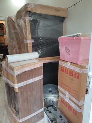 Cartons, wrapped furniture and a storage crate stacked together indoors.