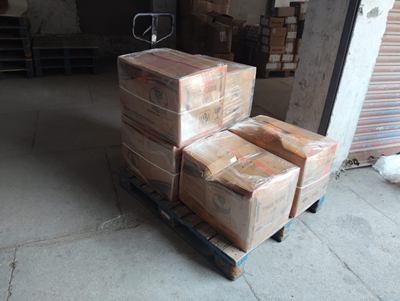 Cartons strapped in stacks on a flat trolley outside a building.