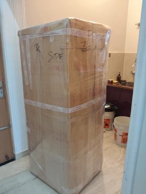 A tall carton wrapped and taped, hand-marked on the side to show which way it stands.