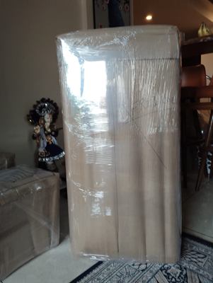 A tall item fully wrapped in film, standing against a wall indoors.