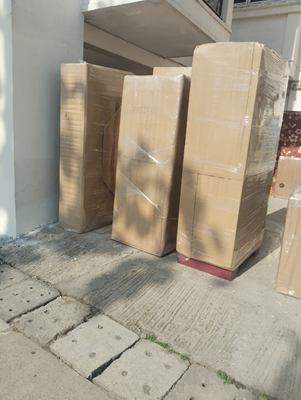 Four tall wrapped items standing on paving outside a building, waiting to be loaded.