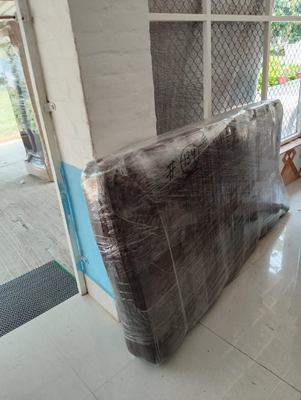 A mattress wrapped in plastic and stood upright against a wall outside.